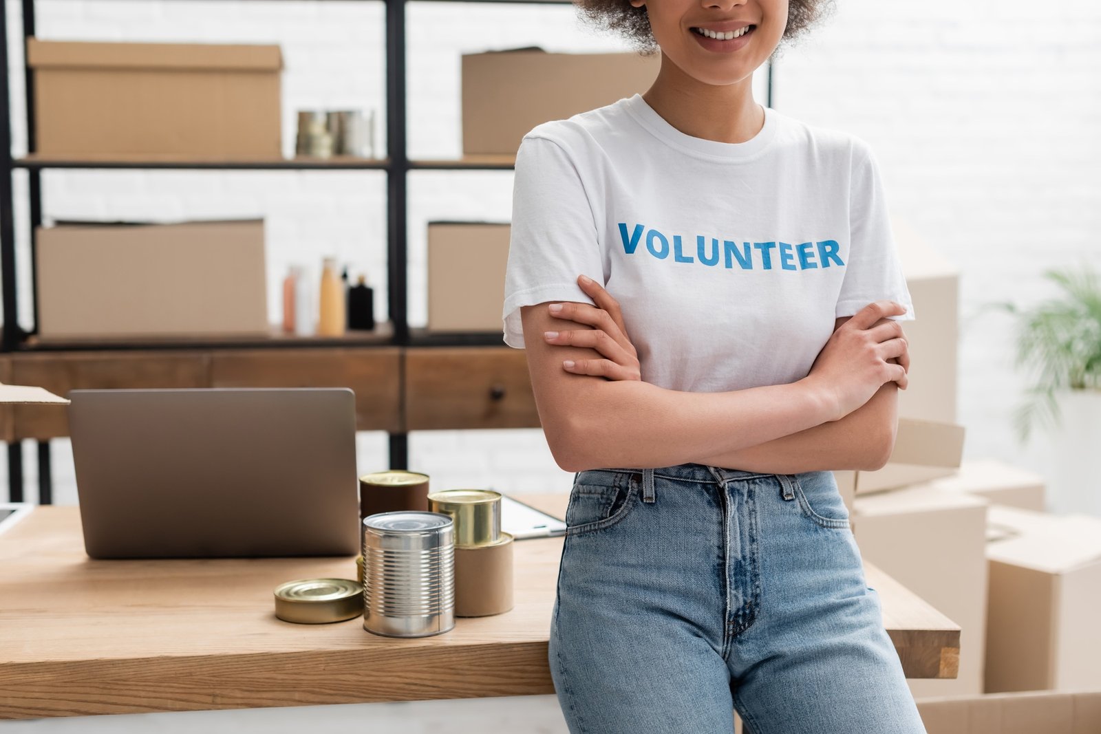 cropped view of african american volunteer standing with crossed arms in charity storehouse